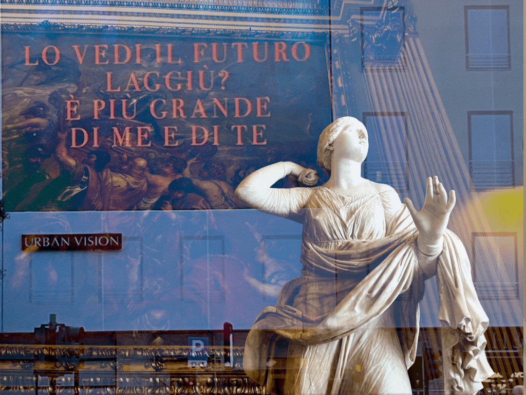 A white Roman statue in front of text reading LO VEDI IL FUTURO, LAGGIU? E PIU GRANDE DI ME E DI TE